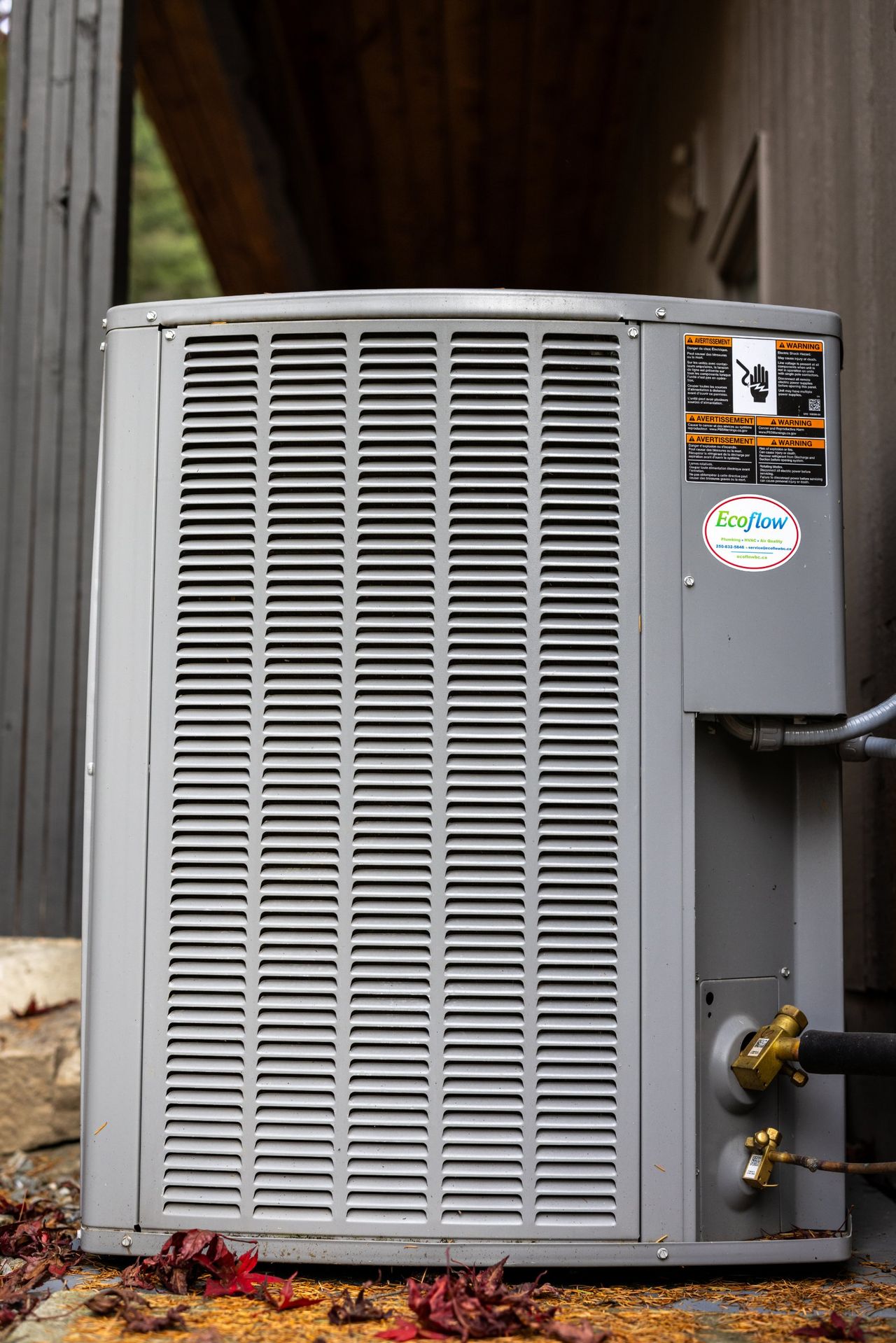 An outdoor air conditioning unit beside a house, with an Ecoflow service sticker on its panel.