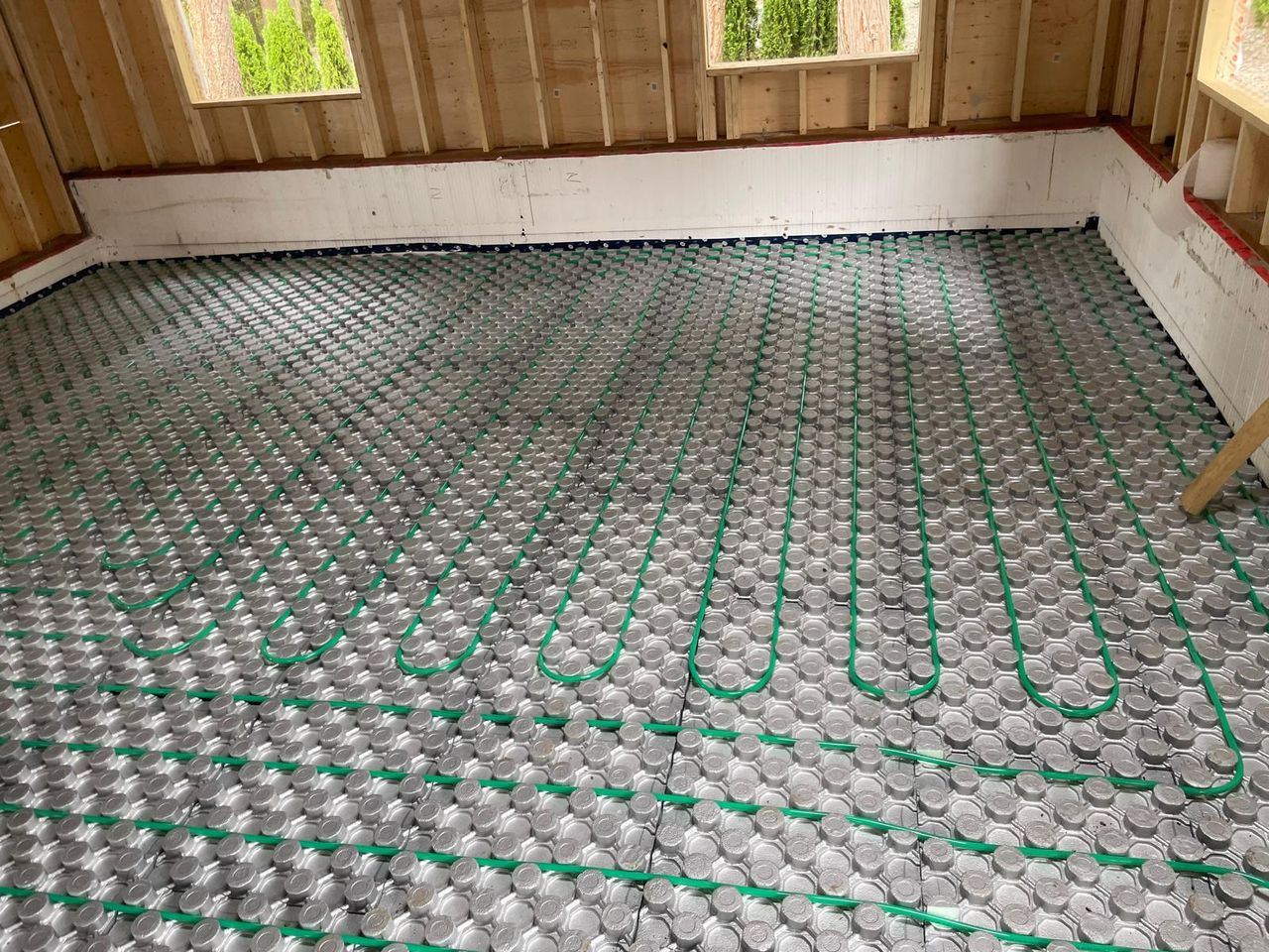 Green in-floor heating tubing clipped into insulated panels across a garage slab, ready for the concrete.