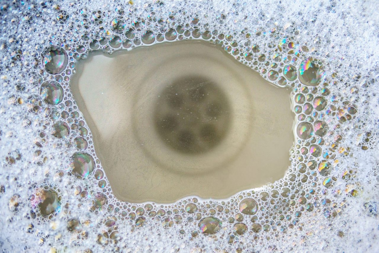 Grey, soapy water sitting over a sink drain that won't go down, ringed with bubbles.