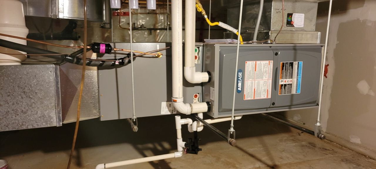 The new high-efficiency AirEase furnace in the same basement, with white plastic venting and a condensate drain.