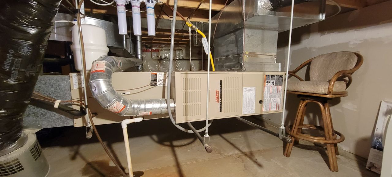 An older Lennox furnace in a basement, venting through a large metal flue pipe.