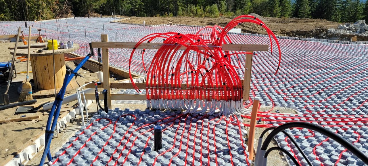 Red PEX tubing run across an insulated panel grid and gathered into a manifold, on a slab waiting to be poured.