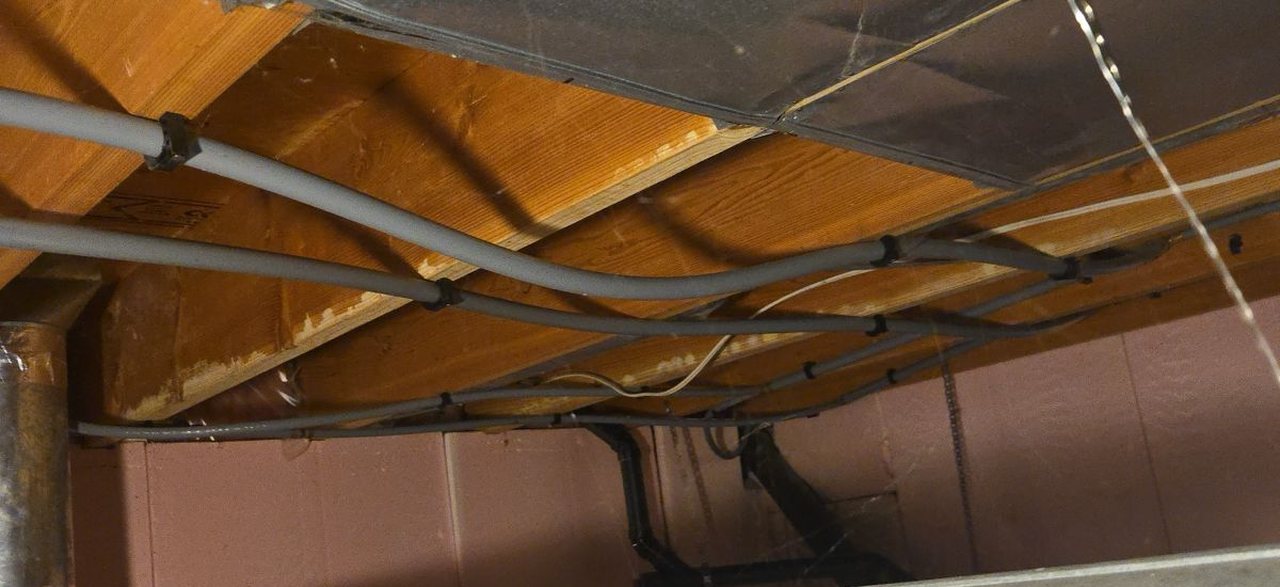 Grey Poly-B supply lines clipped along the floor joists of an unfinished basement, next to ductwork.