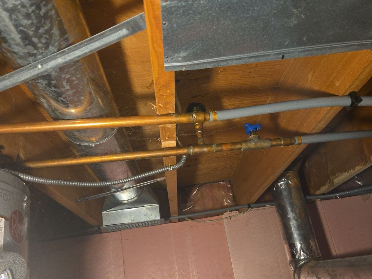 Copper and grey Poly-B supply lines running side by side into brass fittings above a water heater.