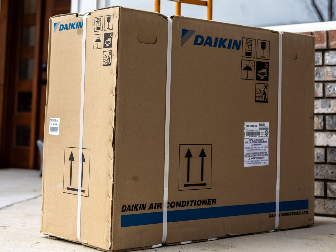 A new Daikin air conditioner, still boxed and strapped, on the front walk of a home ready to go in.