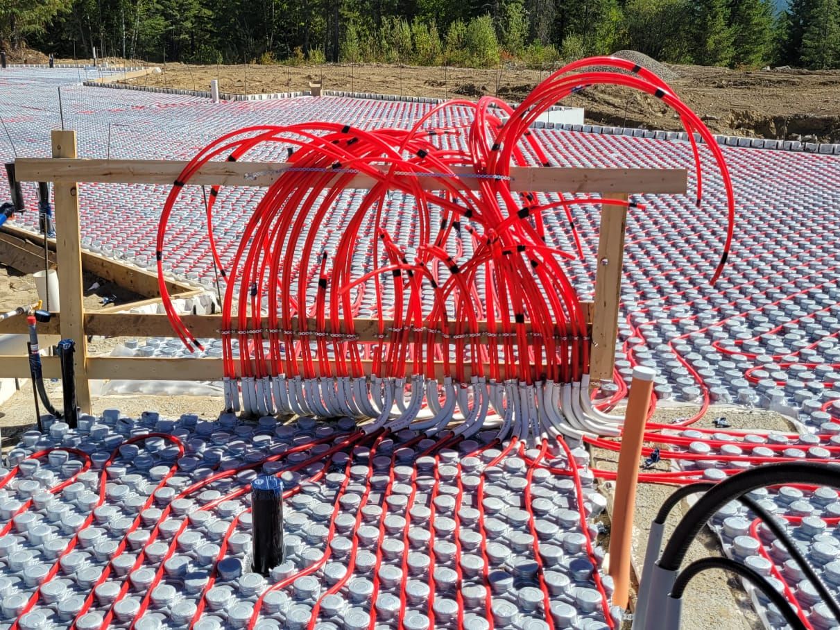 Red in-floor heating loops laid across a new slab, all running back to a manifold frame before the concrete is poured.