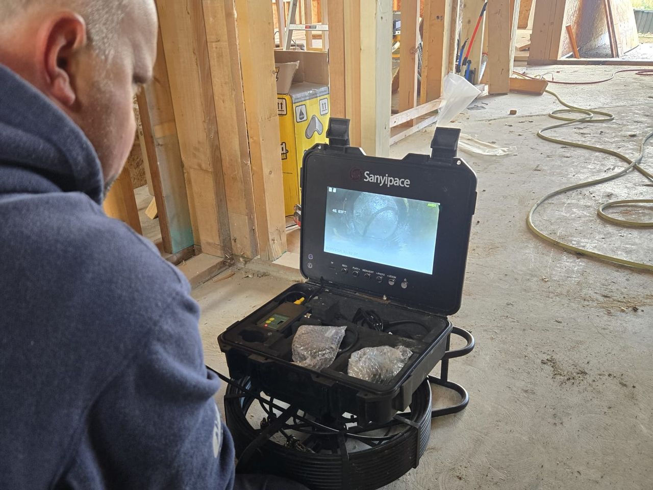 An Ecoflow plumber kneeling on the slab of a house under construction, watching a sewer camera monitor that shows the inside of the drain line, 46 feet in.