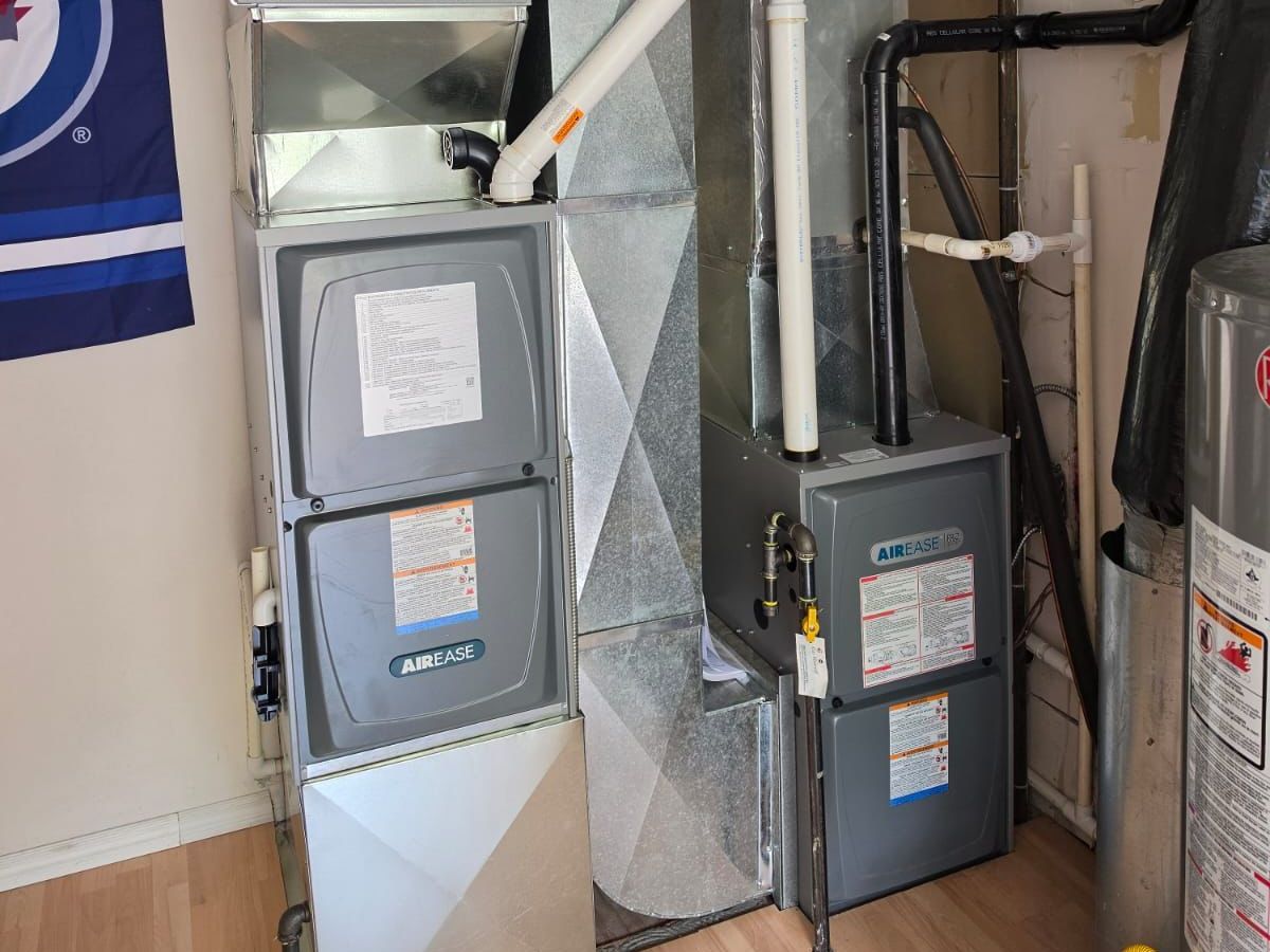 Two Air Ease furnaces installed side by side in a utility room, with their ductwork and white vent pipes.