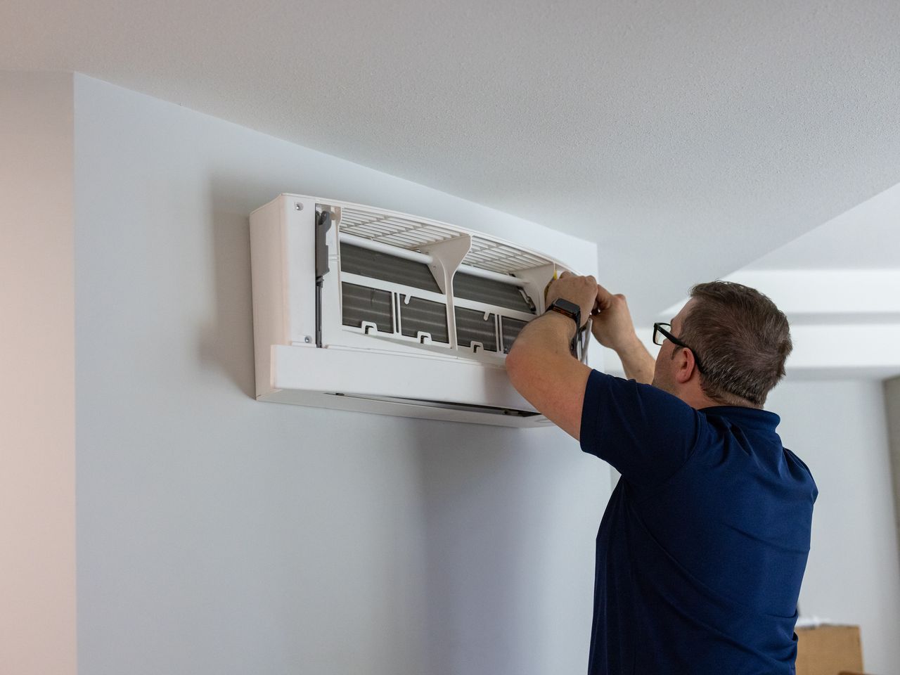 A technician with the front panel open on a ductless mini-split head, working on it where it hangs high on the wall.
