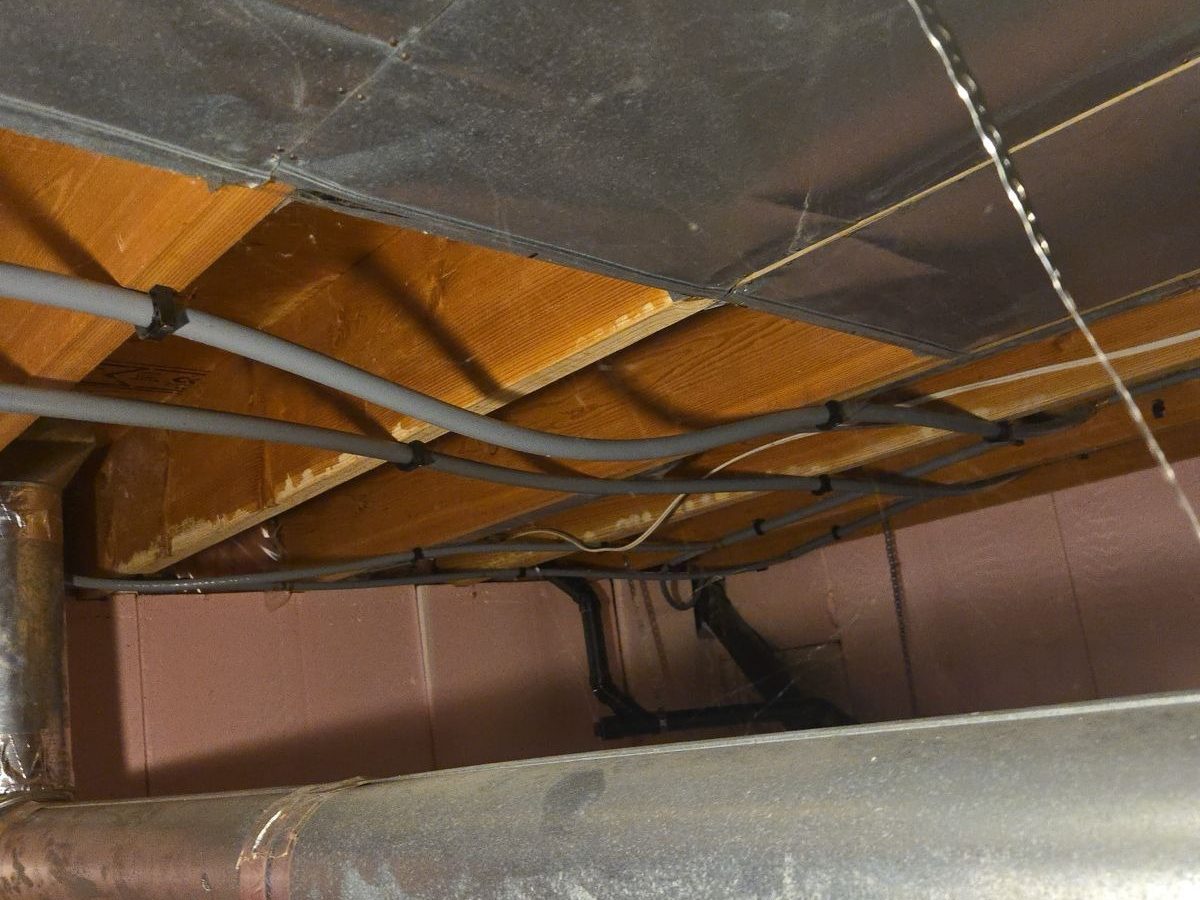 Grey Poly-B supply lines clipped along the floor joists of a basement ceiling, running past the ductwork.