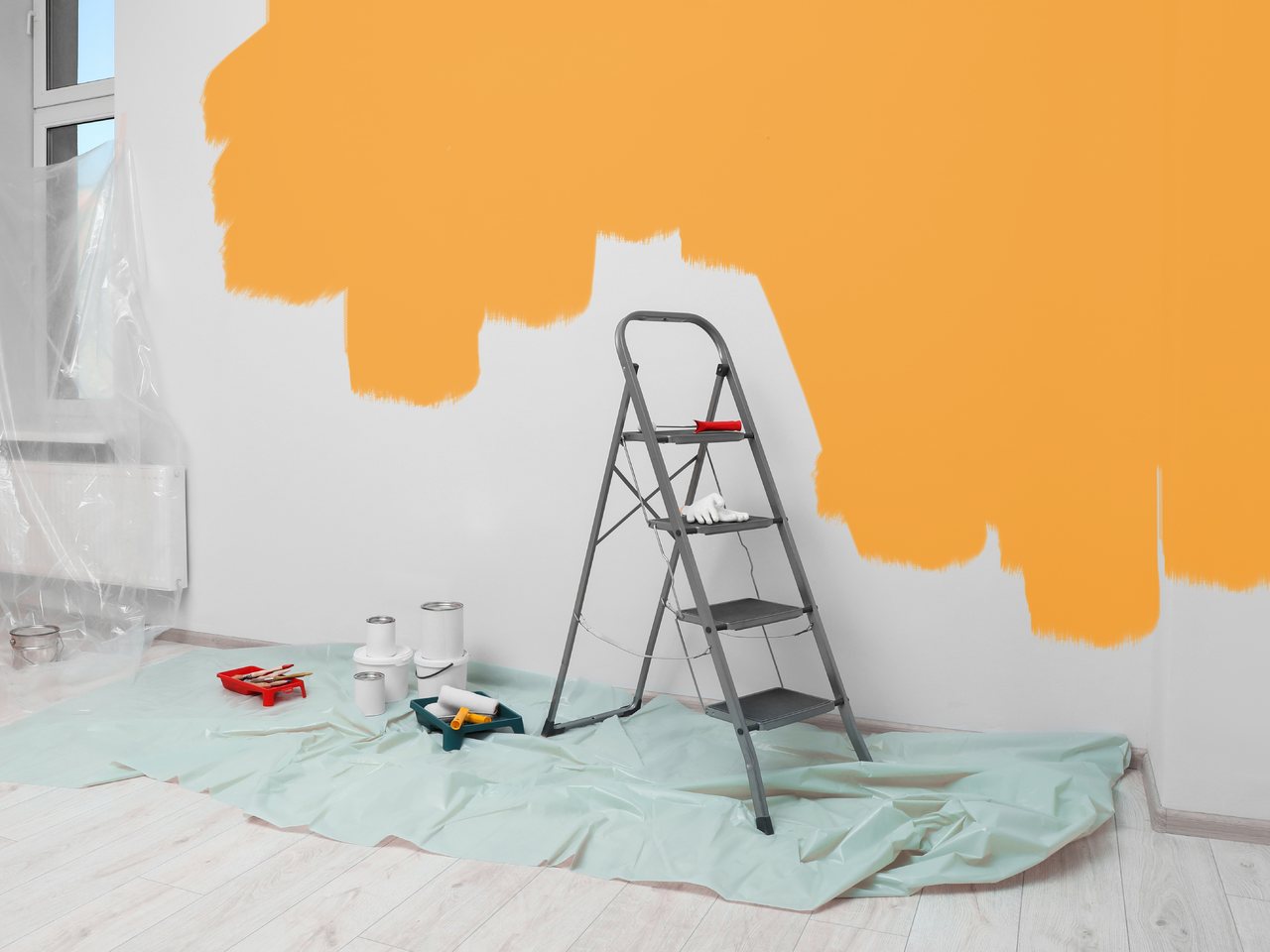 A room part way through a repaint, a stepladder and roller trays standing on a drop sheet against a half-painted wall.