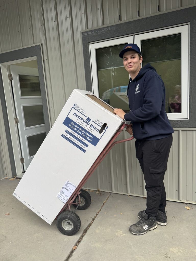 An Ecoflow technician in a company hoodie wheeling a boxed Bradford White electric water heater on a hand truck.